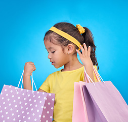 Image showing Girl, shopping and gift bags from birthday party, event or celebration with a present in a studio. Shop choice, bag and little child looking at presents with isolated and blue background with a kid