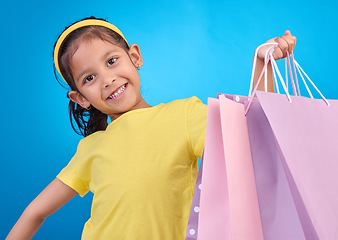 Image showing Girl portrait, shopping and gift bags from birthday party, event or celebration with a present in studio. Shop, bag and happy child looking at presents with isolated and blue background with a kid