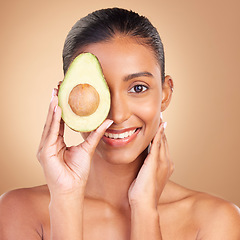 Image showing Portrait, skincare and avocado with a woman in studio on a brown background for natural treatment. Face, food or antioxidants with an attractive young female model holding healthy fruit for nutrition