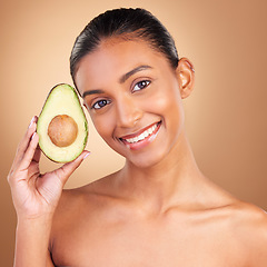 Image showing Portrait, beauty and avocado with a model woman in studio on a brown background for natural treatment. Face, food and antioxidants with an attractive young female holding healthy fruit for nutrition