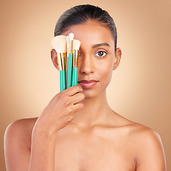 Image showing Makeup, cover and brush with portrait of Indian woman in studio for foundation, blush and self care. Glow, cosmetics and facial with female model on brown background for shine, clean and confidence