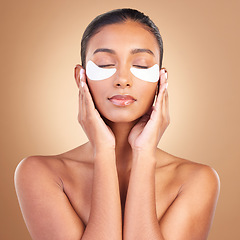 Image showing Skincare, eye patch and touch with Indian woman in studio for facial, spa treatment and glow. Self care, cosmetics and hydration with female model on brown background for mask, product and youth