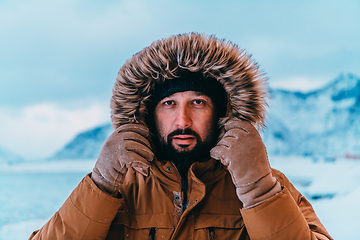 Image showing Headshot photo of a man in a cold snowy area wearing a thick brown winter jacket and gloves. Life in cold regions of the country.