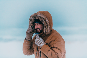 Image showing Headshot photo of a man in a cold snowy area wearing a thick brown winter jacket and gloves. Life in cold regions of the country.