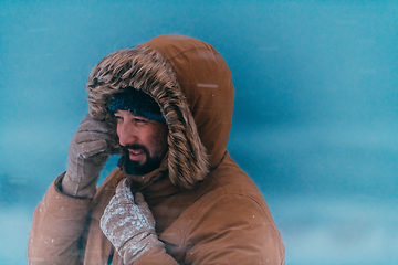 Image showing Headshot photo of a man in a cold snowy area wearing a thick brown winter jacket and gloves. Life in cold regions of the country.