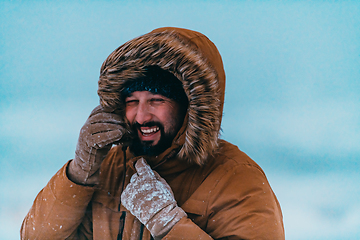 Image showing Headshot photo of a man in a cold snowy area wearing a thick brown winter jacket and gloves. Life in cold regions of the country.