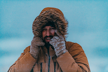 Image showing Headshot photo of a man in a cold snowy area wearing a thick brown winter jacket and gloves. Life in cold regions of the country.