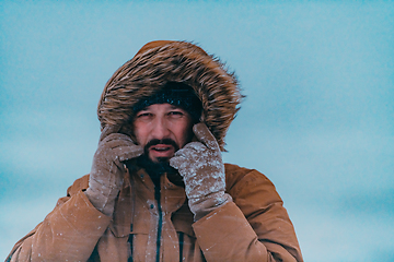 Image showing Headshot photo of a man in a cold snowy area wearing a thick brown winter jacket and gloves. Life in cold regions of the country.