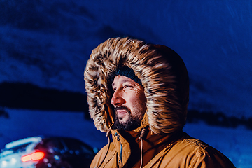 Image showing Head shot of a man in a cold snowy area wearing a thick brown winter jacket, snow goggles and gloves on a cold Scandinavian night. Life in the cold regions of the country.