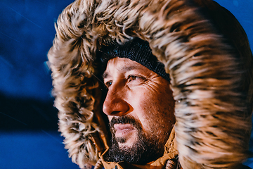 Image showing Head shot of a man in a cold snowy area wearing a thick brown winter jacket, snow goggles and gloves on a cold Scandinavian night. Life in the cold regions of the country.