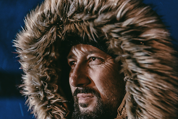 Image showing Head shot of a man in a cold snowy area wearing a thick brown winter jacket, snow goggles and gloves on a cold Scandinavian night. Life in the cold regions of the country.