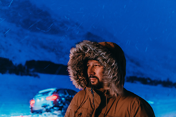 Image showing Head shot of a man in a cold snowy area wearing a thick brown winter jacket, snow goggles and gloves on a cold Scandinavian night. Life in the cold regions of the country.