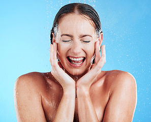 Image showing Shower, water and woman in a studio feeling happy from cleaning and skincare. Wellness, splash and beauty routine of a female model excited from dermatology and self care with blue background