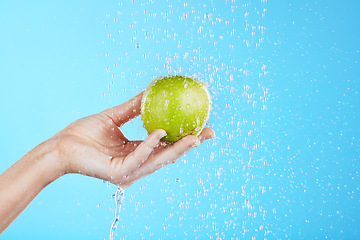 Image showing Water drops, apple cleaning and hands with fruit for wellness, healthcare and self care. Healthy food, green and natural skincare with a hand holding health snack for diet in blue background studio