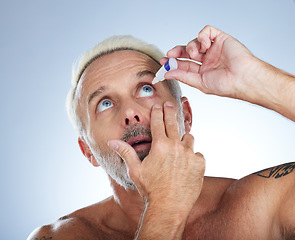 Image showing Eye drops, senior man and studio with medical, healthcare and wellness pharmaceuticals. Isolated, blue background and male model with dry eyes and medicine for vision solution and allergy product