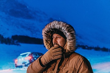 Image showing Head shot of a man in a cold snowy area wearing a thick brown winter jacket, snow goggles and gloves on a cold Scandinavian night. Life in the cold regions of the country.