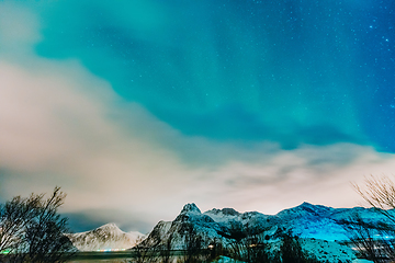 Image showing Amazing display of northern lights seen in the north with a bright green band dancing across the sky with a stunning log cabin lodge below.