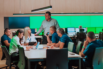 Image showing Group of security guards sitting and having briefing In the system control room They're working in security data center surrounded by multiple Screens