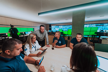 Image showing Group of security guards sitting and having briefing In the system control room They're working in security data center surrounded by multiple Screens