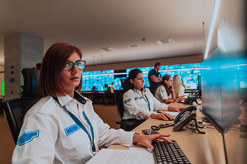 Image showing Group of Security data center operators working in a CCTV monitoring room looking on multiple monitors.Officers Monitoring Multiple Screens for Suspicious Activities