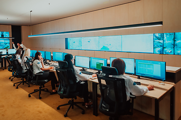 Image showing Group of Security data center operators working in a CCTV monitoring room looking on multiple monitors.Officers Monitoring Multiple Screens for Suspicious Activities