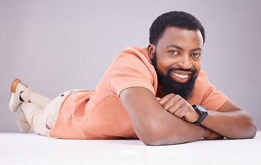 Image showing Portrait, happy and a black man lying on the floor isolated on a grey studio background. Smile, relax and a calm African guy relaxing, smiling and looking confident on the ground of a backdrop