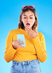 Image showing Notification, shocked and woman surprised by phone due to trending social media news isolated in a studio blue background. Wow, omg and young female amazed by a cellphone using internet or online