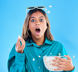 Image showing 3D glasses, popcorn and wow with a woman in studio on a blue background looking shocked while eating a snack. Portrait, movie and video entertainment with an attractive young female feeling surprised