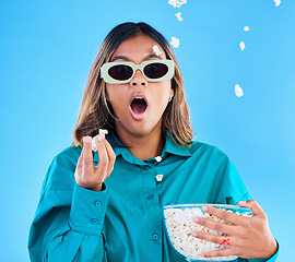 Image showing 3D movie, popcorn and surprise with a woman in studio on a blue background looking shocked while eating a snack. Portrait, glasses and wow with an attractive young female watching video entertainment