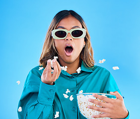 Image showing 3D movie, popcorn and wow with a woman in studio on a blue background looking shocked while eating a snack. Portrait, glasses and video entertainment with an attractive young female feeling surprised