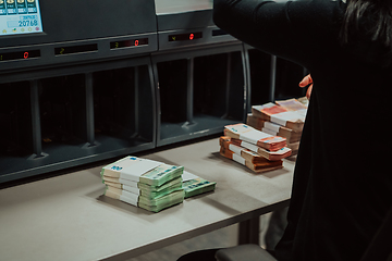 Image showing Bank employees using money counting machine while sorting and counting paper banknotes inside bank vault. Large amounts of money in the bank