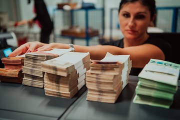 Image showing Bank employees using money counting machine while sorting and counting paper banknotes inside bank vault. Large amounts of money in the bank