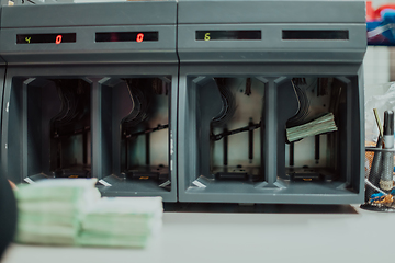 Image showing Bank employees using money counting machine while sorting and counting paper banknotes inside bank vault. Large amounts of money in the bank