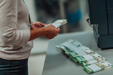 Image showing Bank employees using money counting machine while sorting and counting paper banknotes inside bank vault. Large amounts of money in the bank