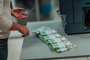 Image showing Bank employees using money counting machine while sorting and counting paper banknotes inside bank vault. Large amounts of money in the bank