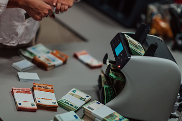 Image showing Bank employees using money counting machine while sorting and counting paper banknotes inside bank vault. Large amounts of money in the bank