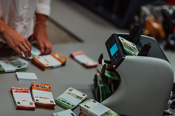 Image showing Bank employees using money counting machine while sorting and counting paper banknotes inside bank vault. Large amounts of money in the bank