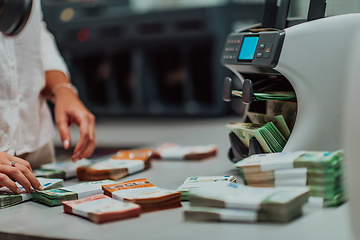 Image showing Bank employees using money counting machine while sorting and counting paper banknotes inside bank vault. Large amounts of money in the bank