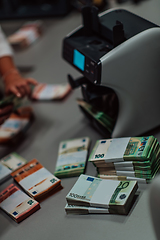 Image showing Bank employees using money counting machine while sorting and counting paper banknotes inside bank vault. Large amounts of money in the bank