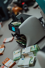 Image showing Bank employees using money counting machine while sorting and counting paper banknotes inside bank vault. Large amounts of money in the bank