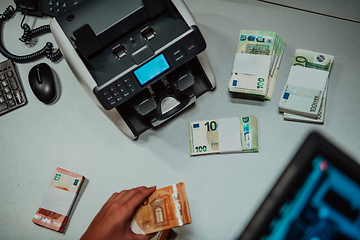 Image showing Bank employees using money counting machine while sorting and counting paper banknotes inside bank vault. Large amounts of money in the bank