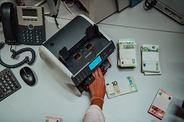 Image showing Bank employees using money counting machine while sorting and counting paper banknotes inside bank vault. Large amounts of money in the bank