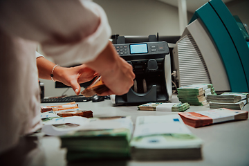 Image showing Bank employees using money counting machine while sorting and counting paper banknotes inside bank vault. Large amounts of money in the bank