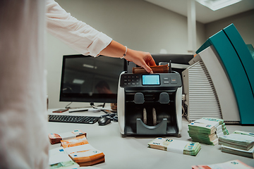 Image showing Bank employees using money counting machine while sorting and counting paper banknotes inside bank vault. Large amounts of money in the bank