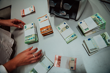 Image showing Bank employees using money counting machine while sorting and counting paper banknotes inside bank vault. Large amounts of money in the bank