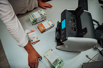 Image showing Bank employees using money counting machine while sorting and counting paper banknotes inside bank vault. Large amounts of money in the bank