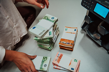 Image showing Bank employees using money counting machine while sorting and counting paper banknotes inside bank vault. Large amounts of money in the bank