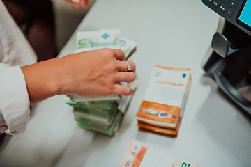 Image showing Bank employees using money counting machine while sorting and counting paper banknotes inside bank vault. Large amounts of money in the bank