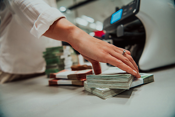 Image showing Bank employees using money counting machine while sorting and counting paper banknotes inside bank vault. Large amounts of money in the bank