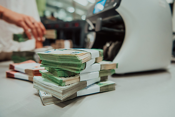 Image showing Bank employees using money counting machine while sorting and counting paper banknotes inside bank vault. Large amounts of money in the bank